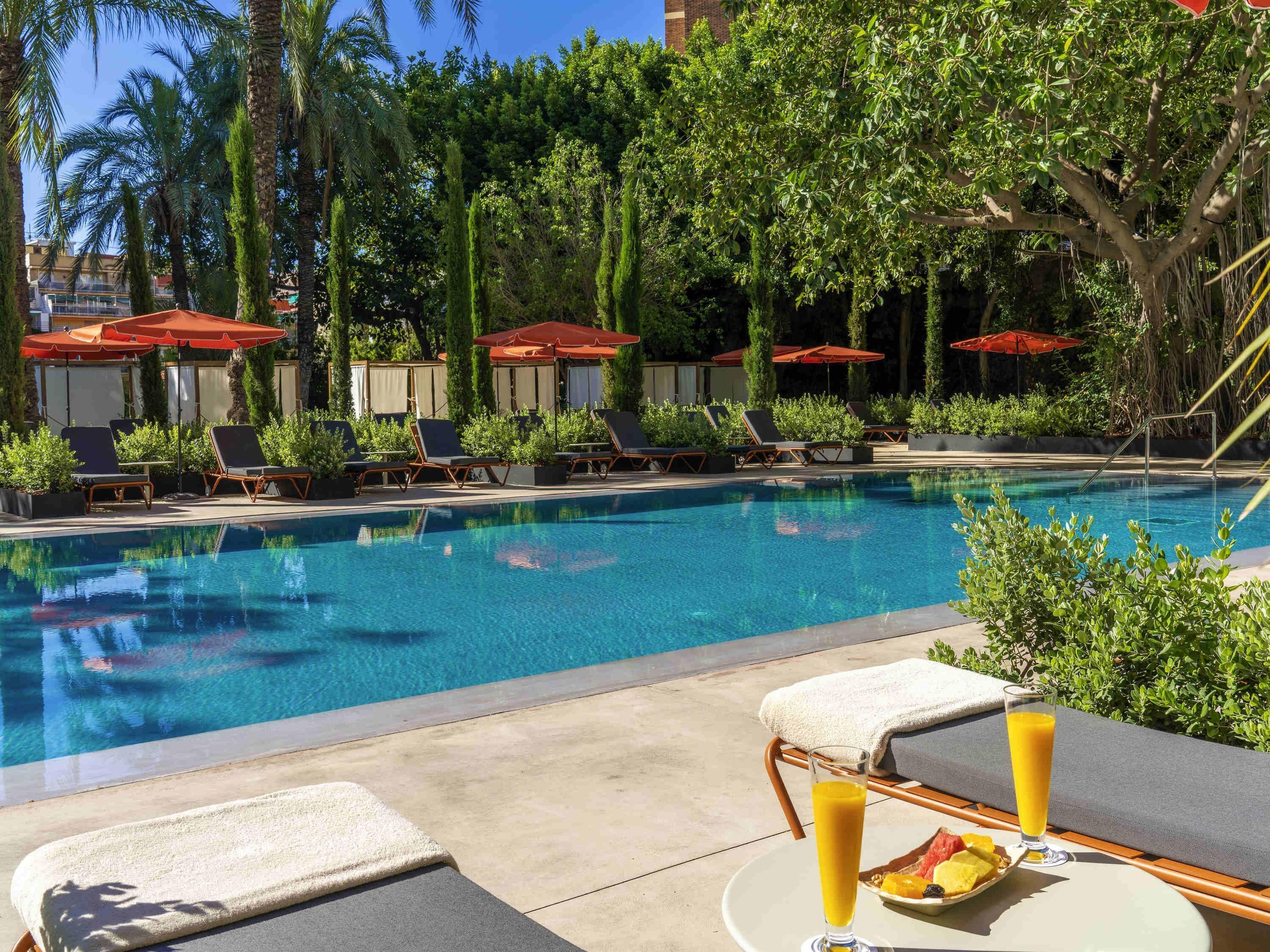 Área de piscina com espreguiçadeiras, guarda-sóis e uma mesa com bebida e frutas.