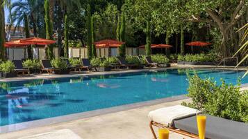 A poolside area with lounge chairs, umbrellas, and a table with a drink and fruit.