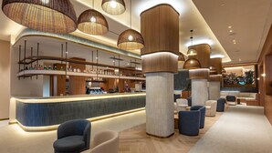 Zona de bar moderna con una barra curva, lámparas de mimbre colgantes y asientos sobre suelo de madera.