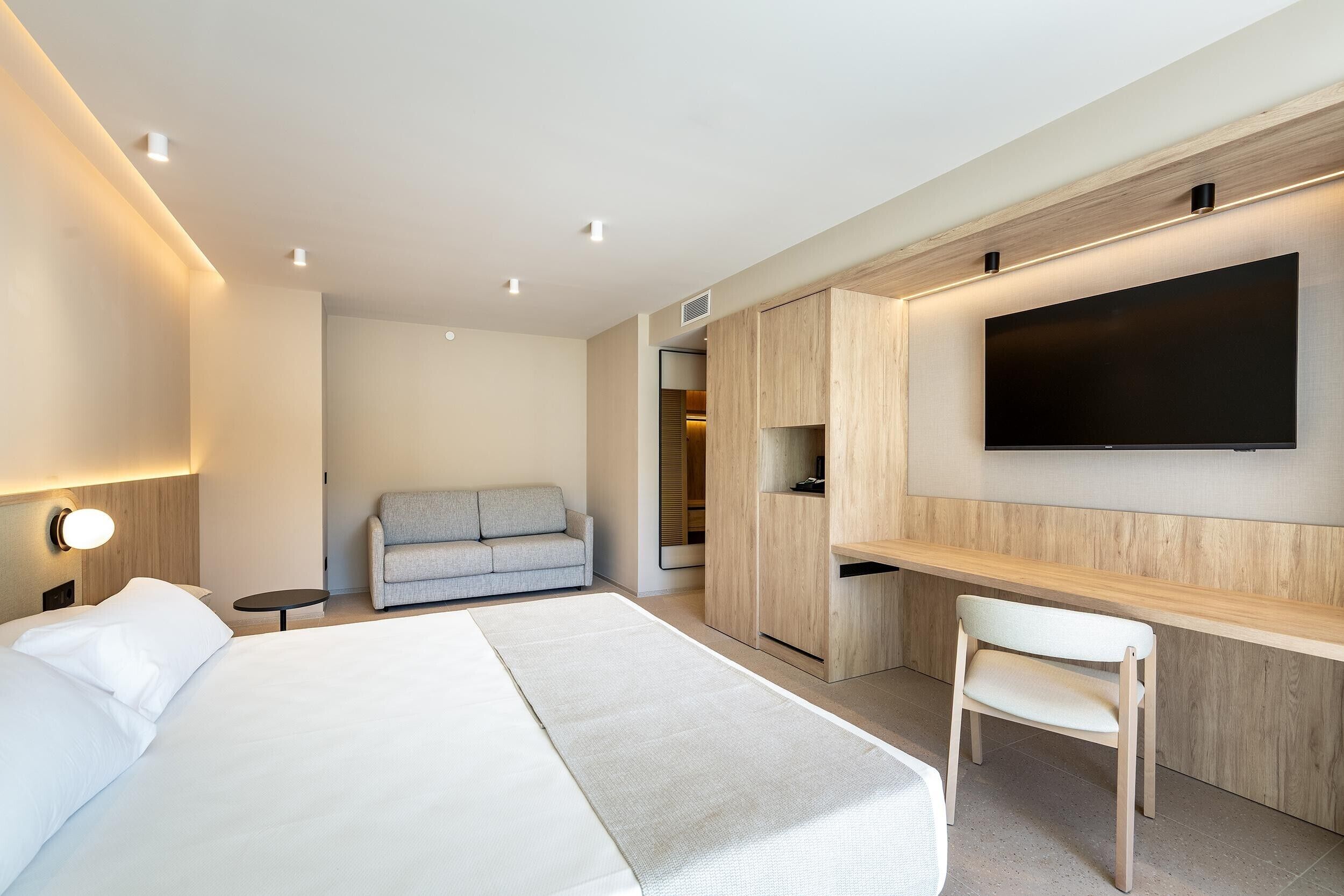 Una habitación de hotel moderna con cama, sofá, escritorio y televisión.