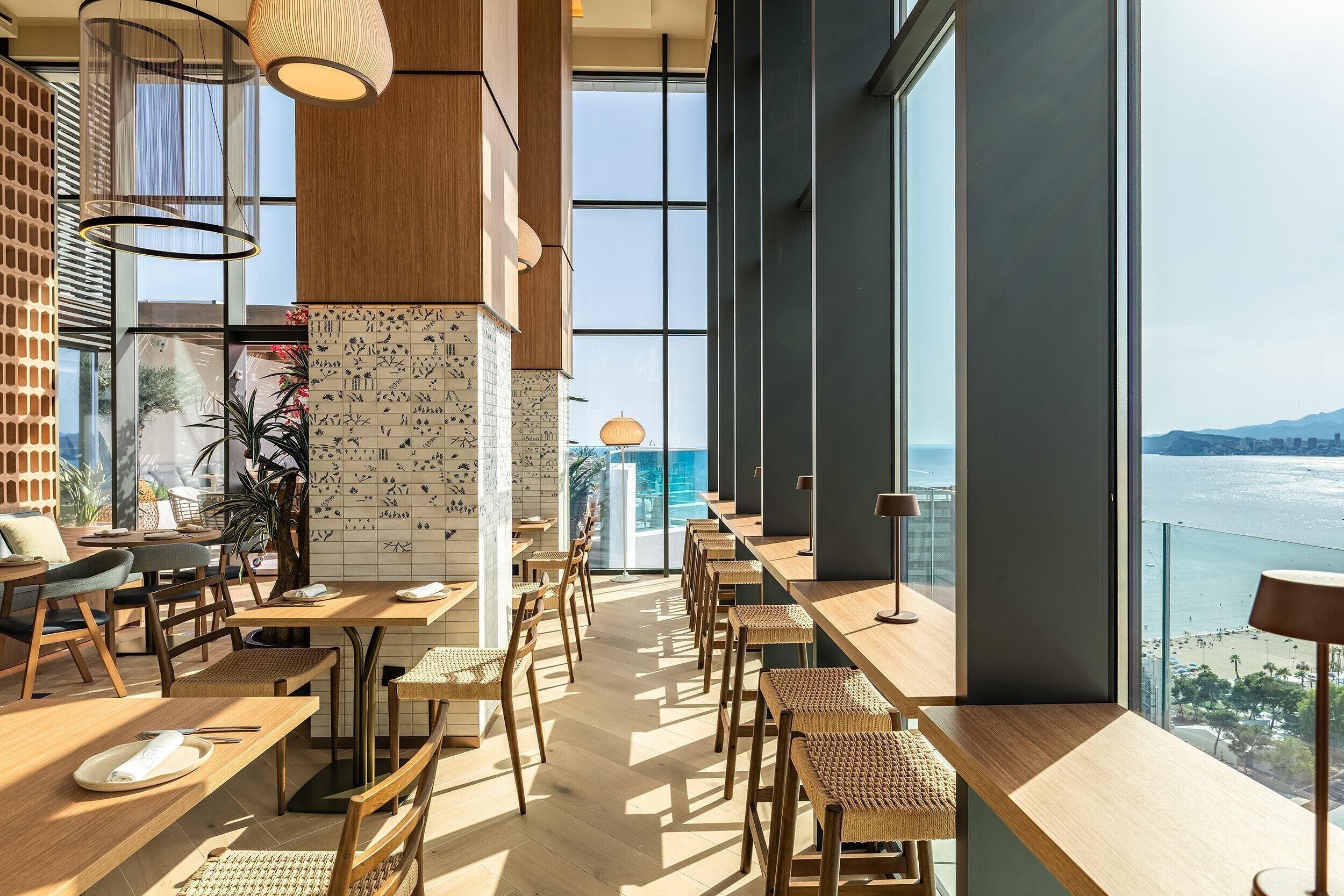 Un restaurant moderne avec de hauts plafonds, de grandes fenêtres et une vue sur la mer.
