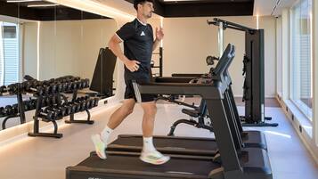 A person running on a treadmill in a gym with weightlifting equipment and dumbbells.