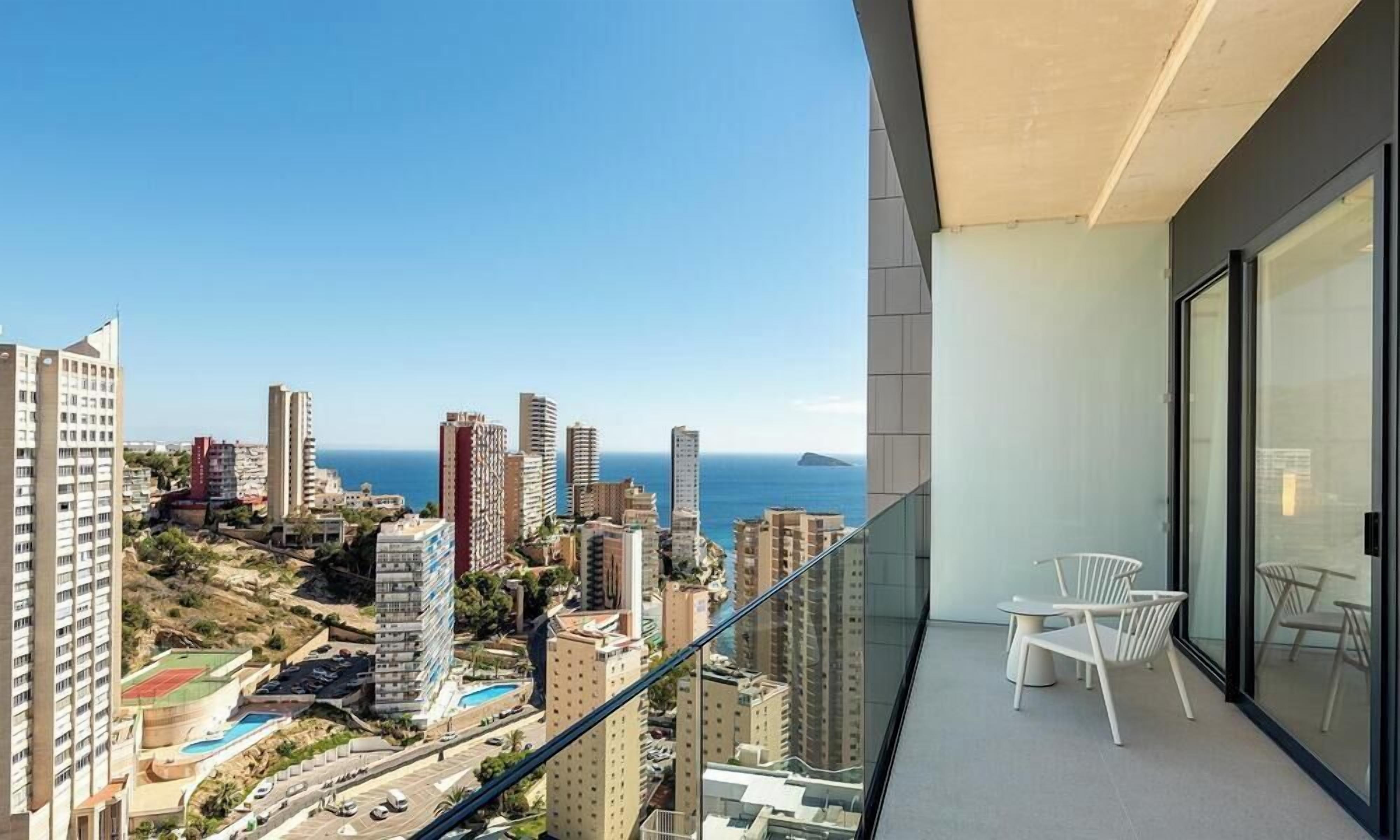 A balcony with a city view, a glass door, and a white chair.