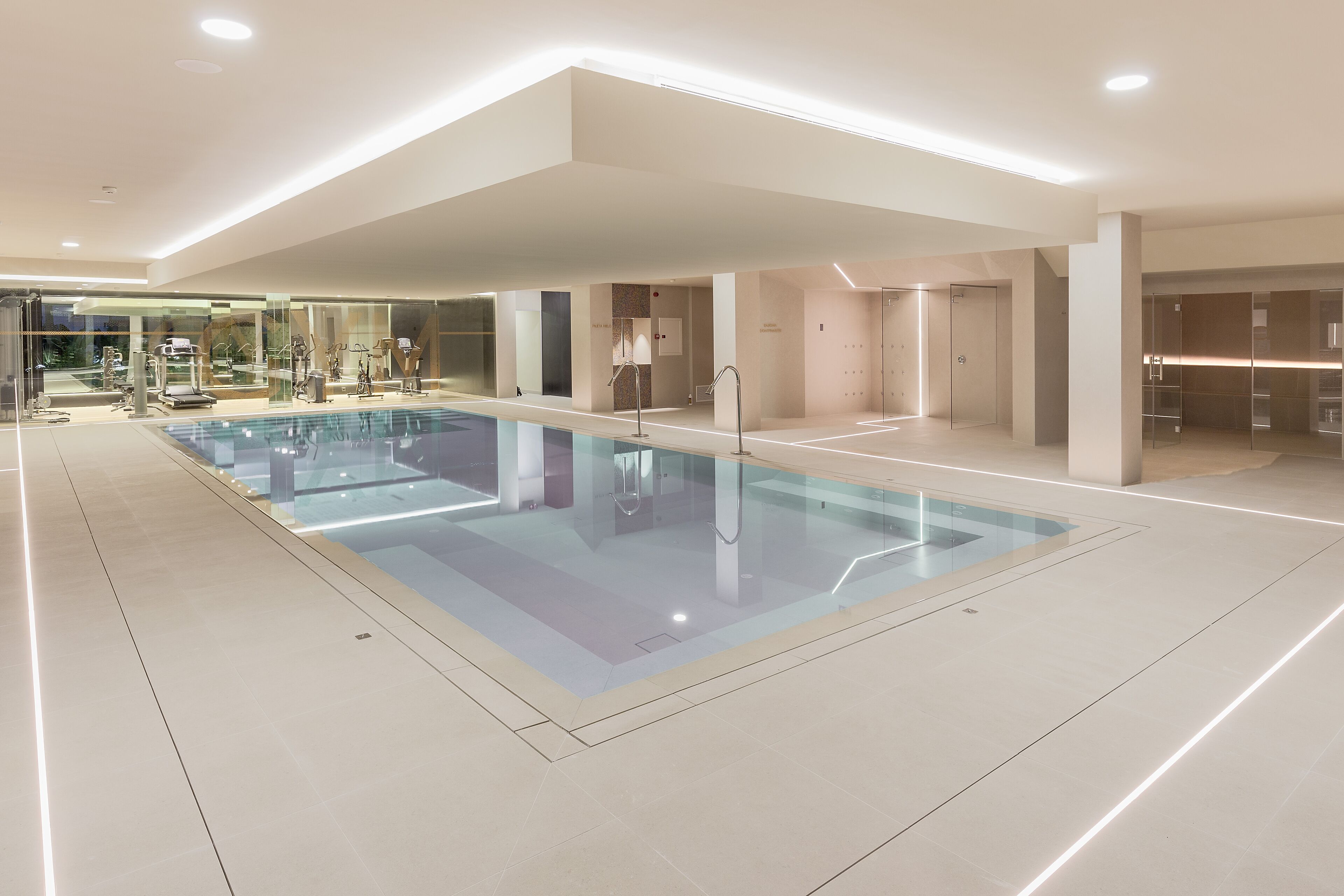 A modern indoor swimming pool with glass walls, a clean, minimalist design, and a spacious layout.