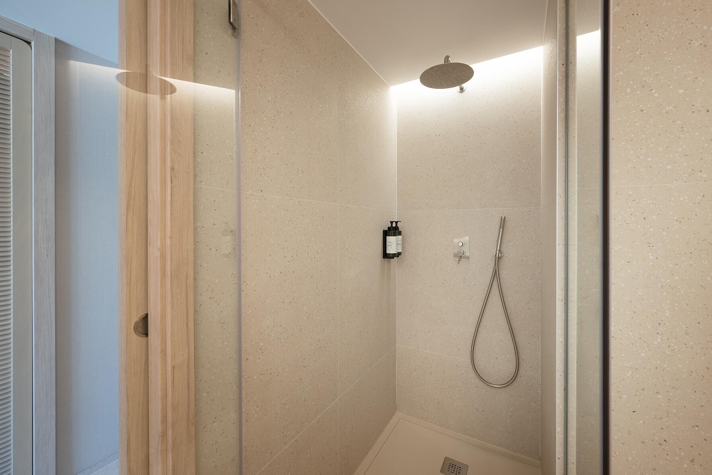 Una ducha moderna con un cabezal de ducha de mano y un panel de control en la pared.