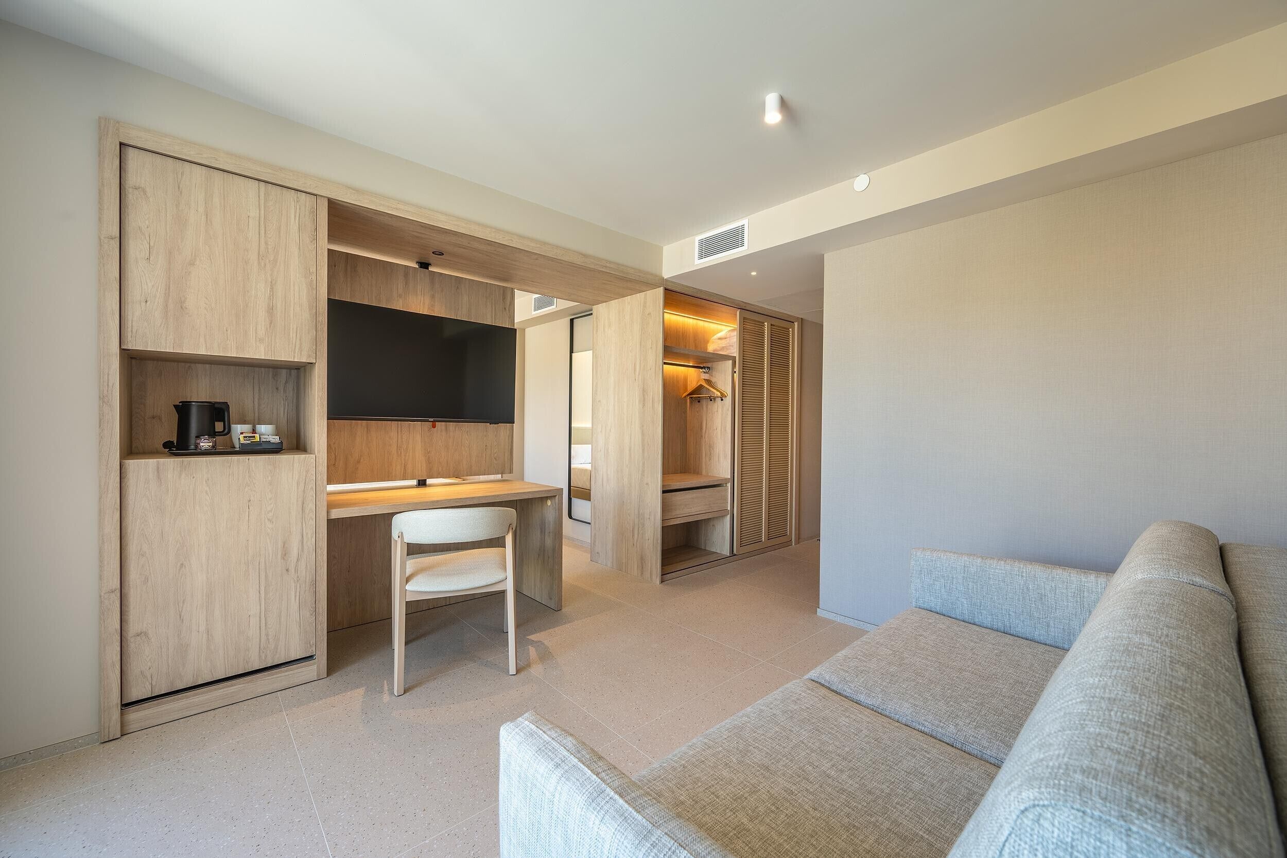 Una habitación moderna con escritorio integrado, una silla, televisor y armario.