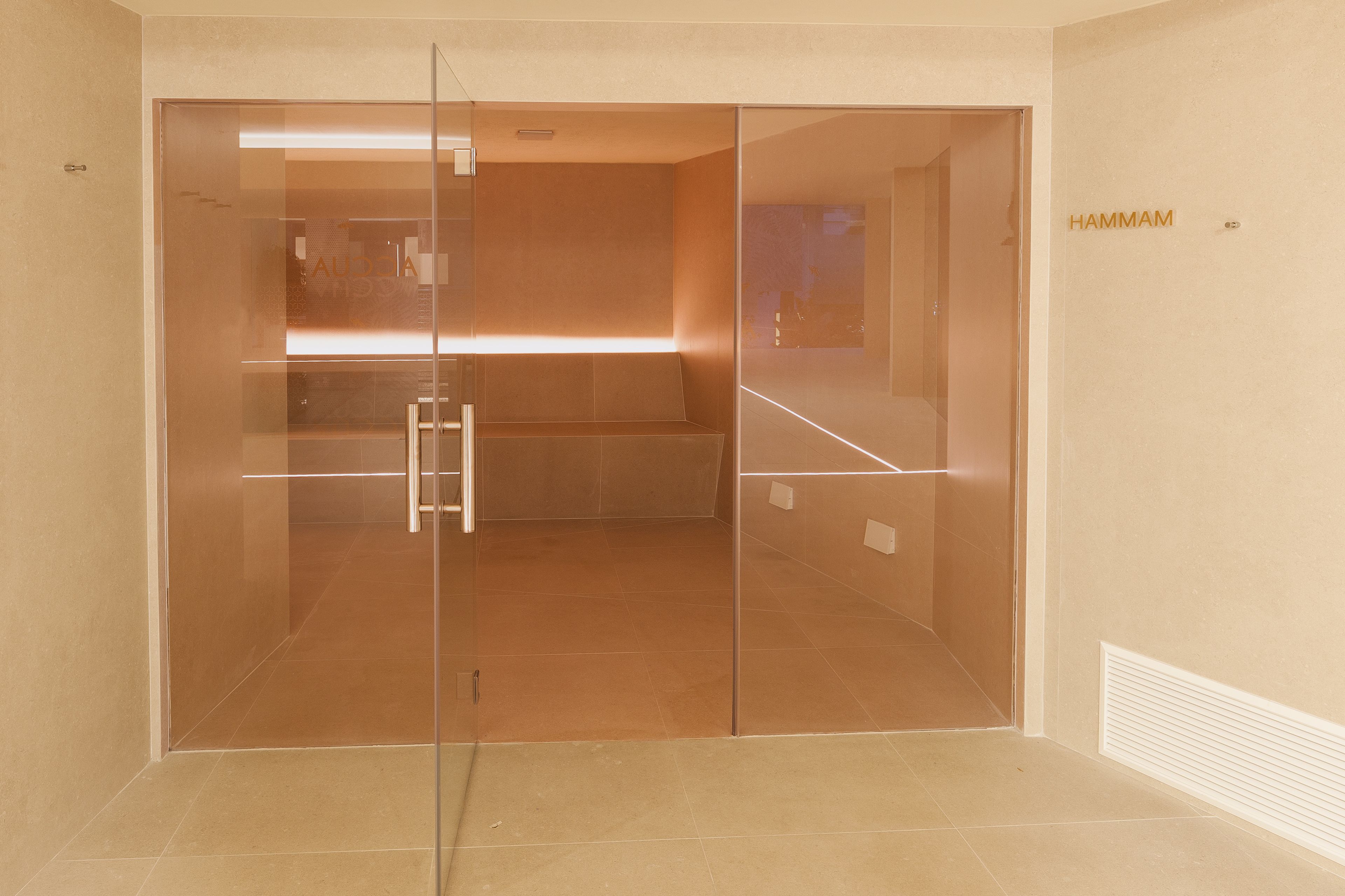 A modern, empty room with a glass door, a bench, and a sign reading "HAMMAM".