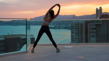A person stretching on a balcony with a cityscape and mountains in the background.