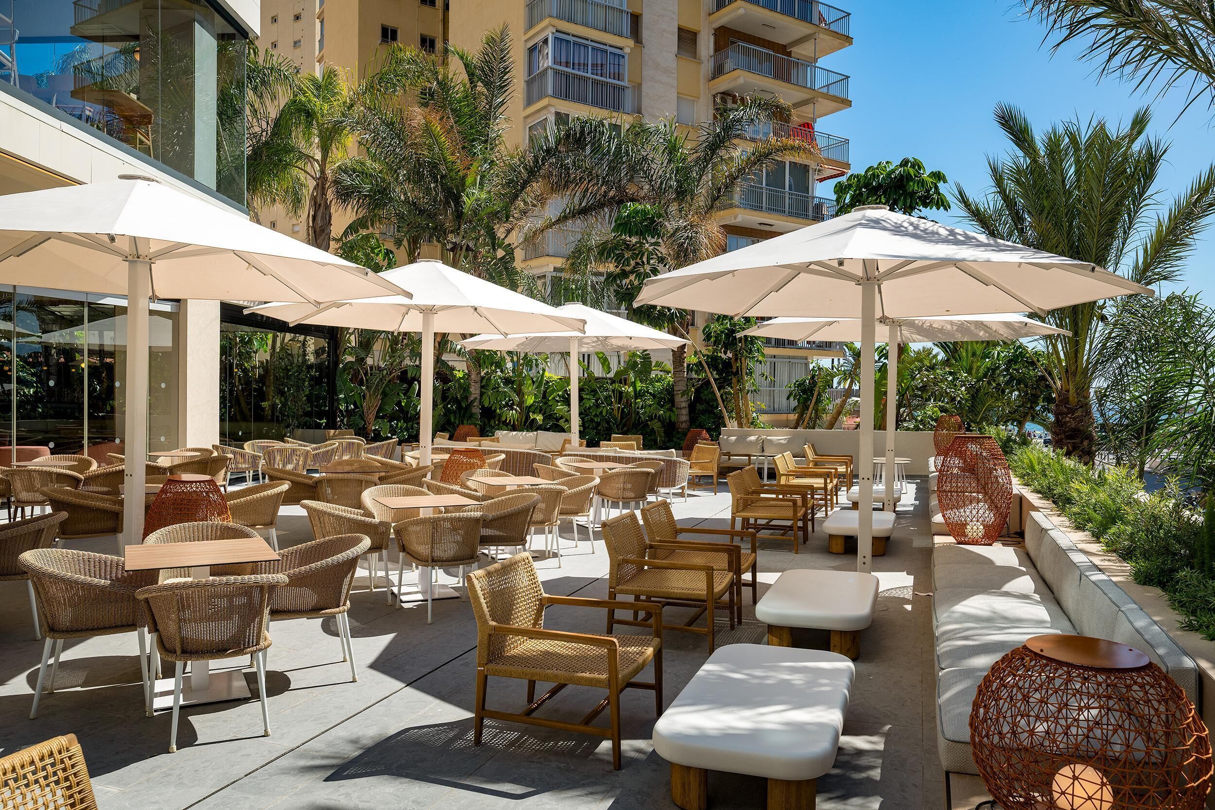 Outdoor seating with umbrellas, wicker chairs, and a poolside area with palm trees.