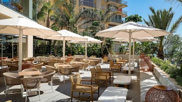 Outdoor seating with umbrellas, wicker chairs, and a poolside area with palm trees.
