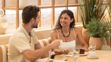 A couple seated at a table with a cup of coffee, a slice of cake, and a glass of water.