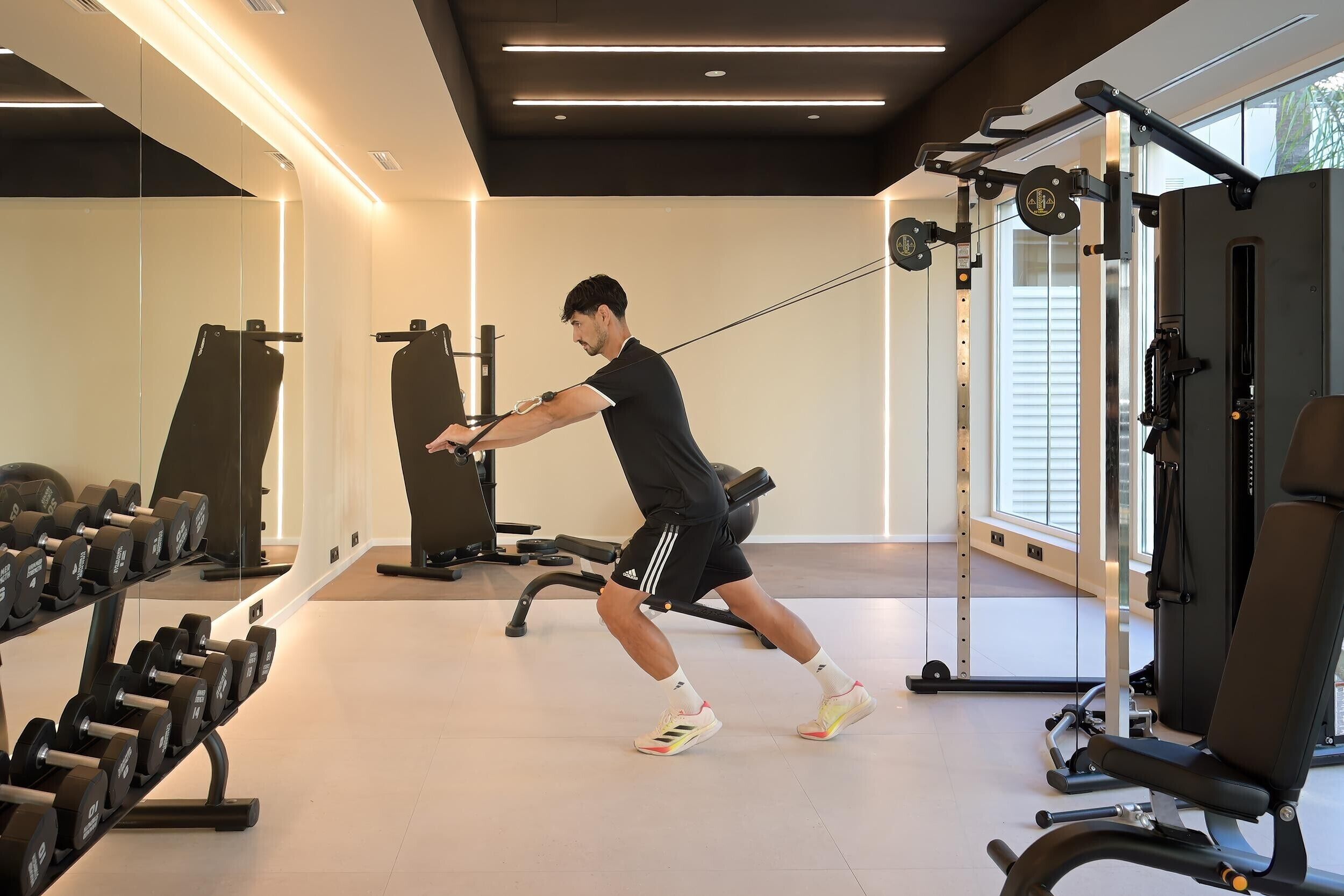 A man performing a cable exercise in a gym with weight racks and exercise equipment.