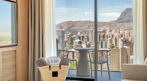 Un balcon avec vue sur la ville et les montagnes, une table avec des chaises et un panier contenant des serviettes.