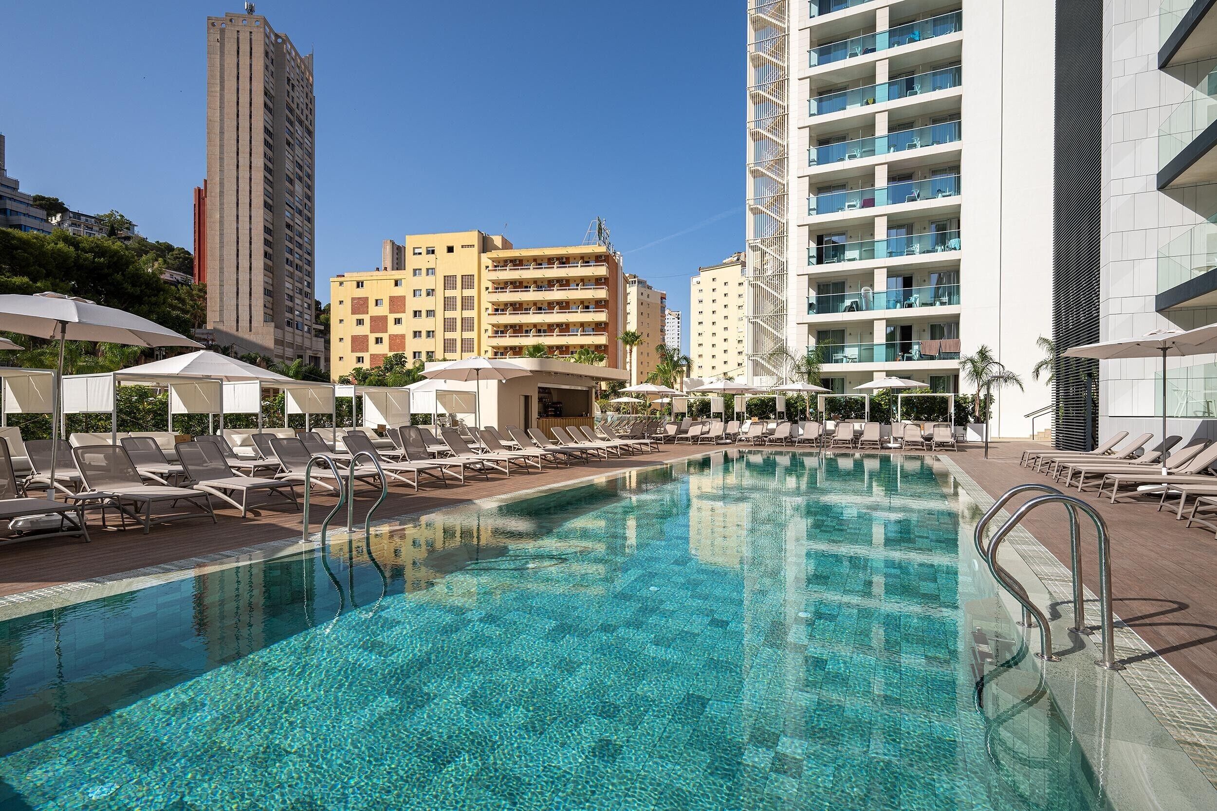 A swimming pool with lounge chairs and umbrellas, surrounded by high-rise buildings.