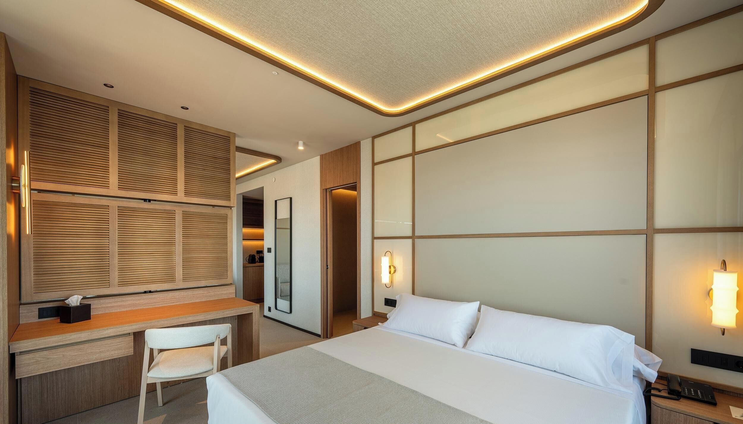 Habitación de hotel con cama, escritorio, silla e iluminación en la pared.