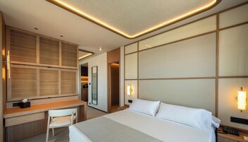 Habitación de hotel con cama, escritorio, silla e iluminación en la pared.