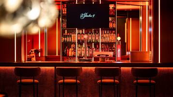 Zona de bar con un letrero de neón que dice 'Studio 4', estantes llenos de licores y tres taburetes de bar.