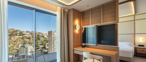 A modern hotel room with a large window, a desk, a bed, and a TV.