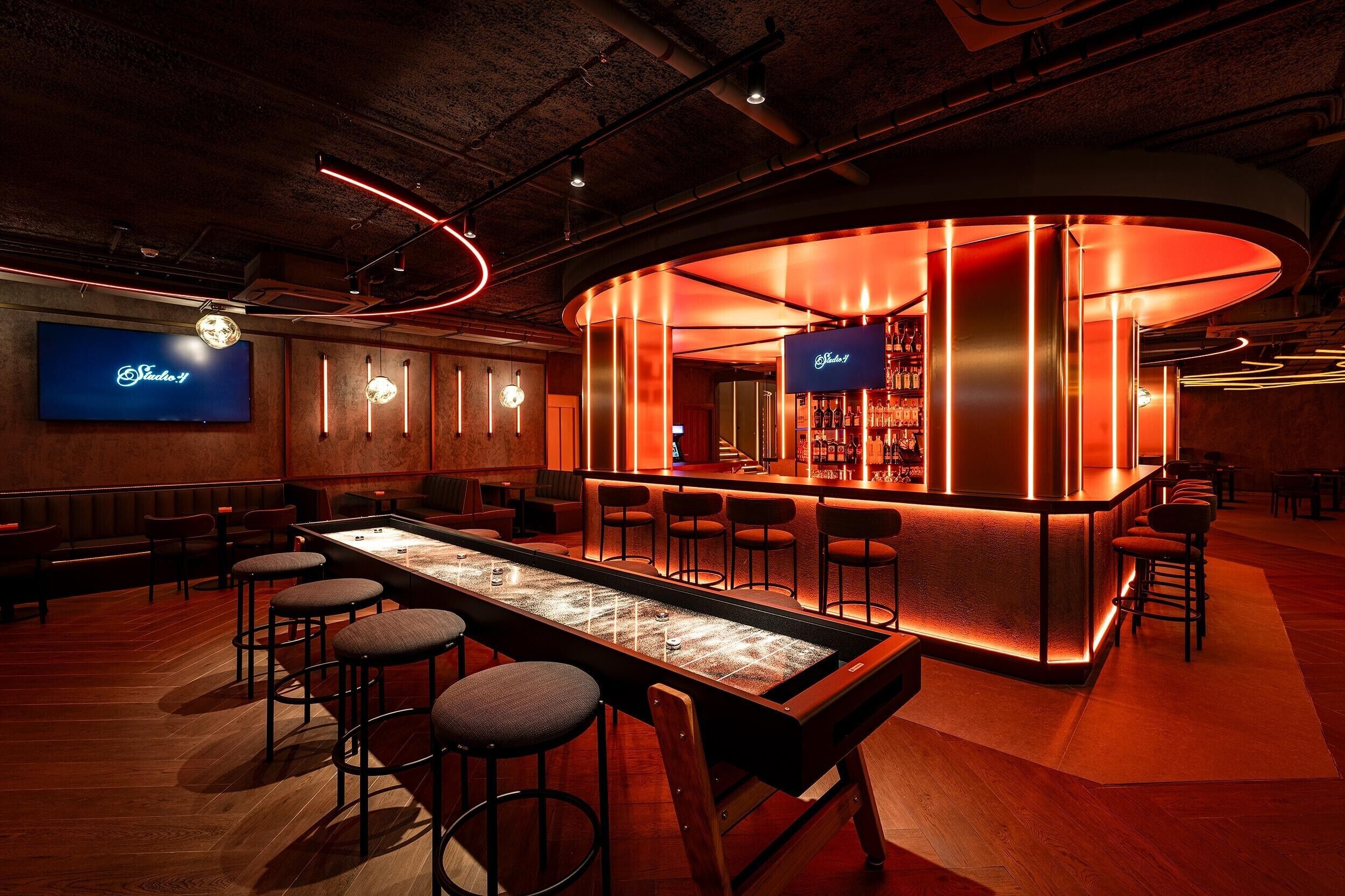 Un'area bar con un lungo bancone, sgabelli e uno schermo televisivo che mostra 'Studio 11'.