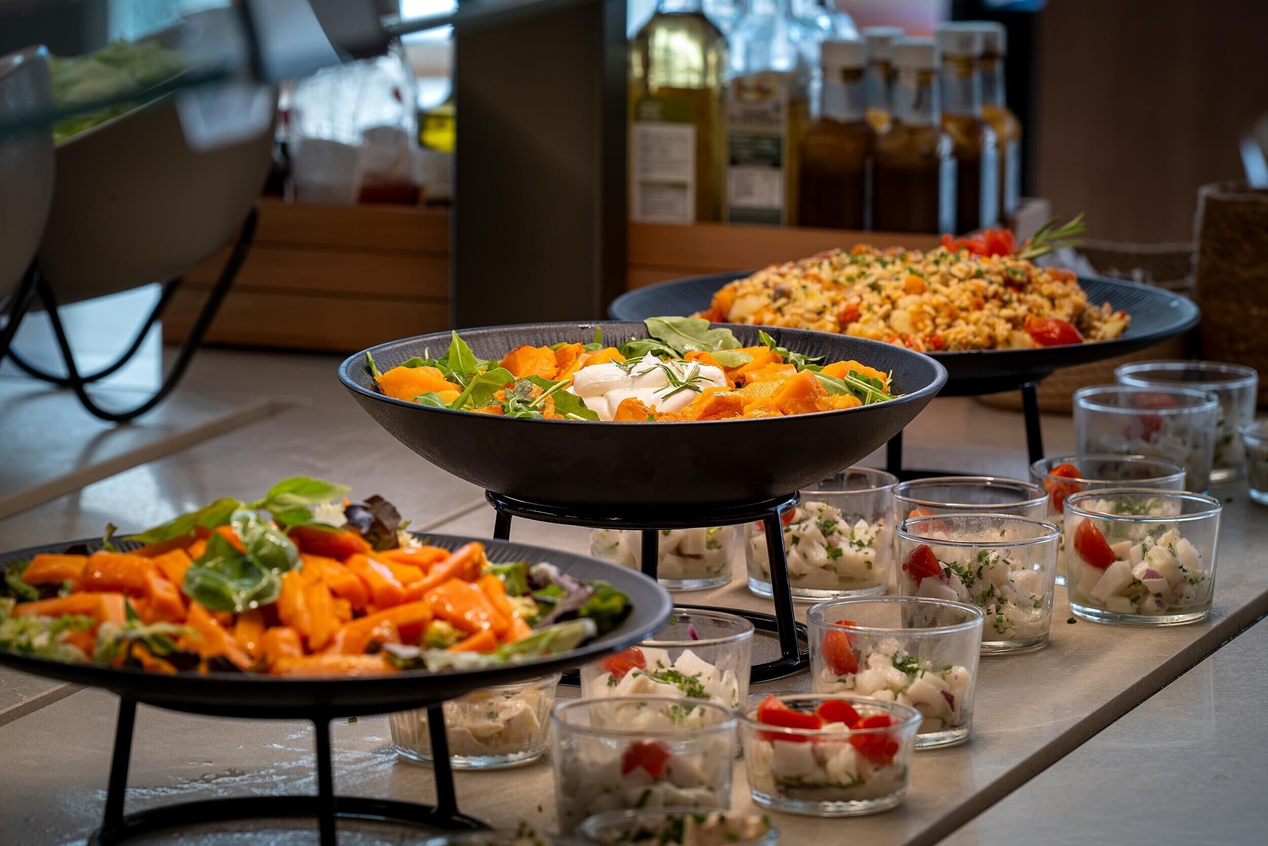 Una mesa de buffet con diversos platos, incluyendo un bol de ensalada, un plato de verduras y varios recipientes pequeños de aperitivos.