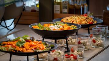 Una mesa de buffet con diversos platos, incluyendo un bol de ensalada, un plato de verduras y varios recipientes pequeños de aperitivos.