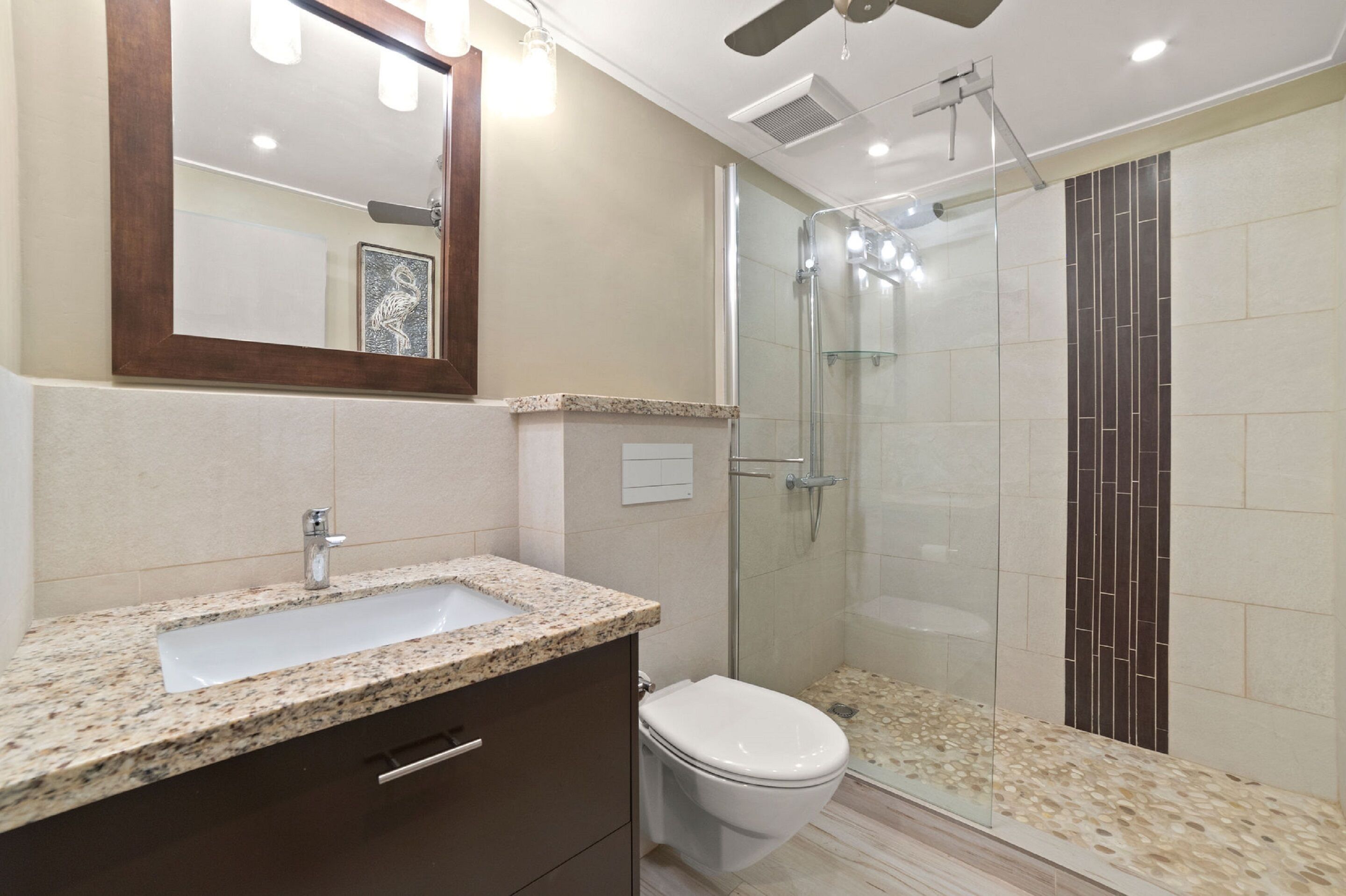 A modern bathroom with a granite countertop sink, a white toilet, and a glass-enclosed shower.