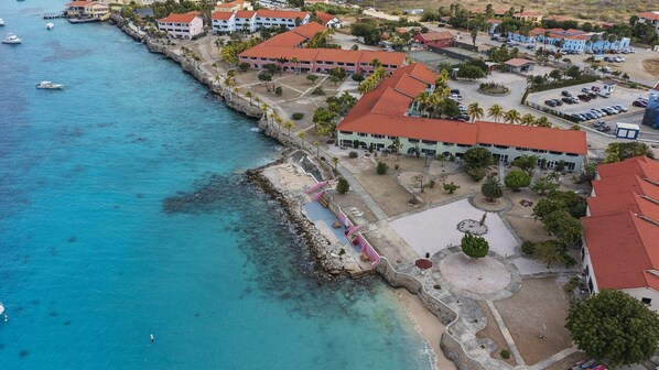An aerial view of a coastal area with buildings, a pier, and clear blue waters. - Sand Dollar Bonaire (Kralendijk)