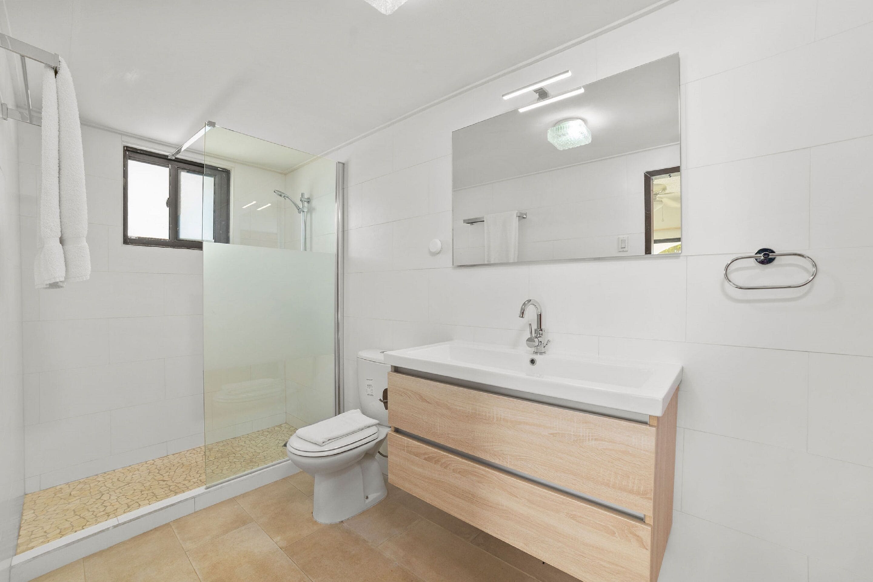 Un baño moderno con cabina de ducha de vidrio, inodoro, lavabo con espejo y un perchero para toallas.