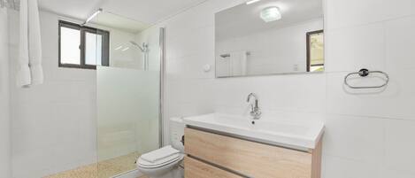Un baño moderno con cabina de ducha de vidrio, inodoro, lavabo con espejo y un perchero para toallas.