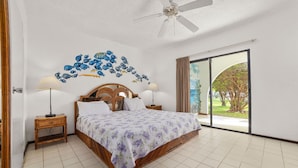 A bedroom with a bed, two bedside tables, a ceiling fan, and a view of the outdoors. - Sand Dollar Bonaire (Kralendijk)