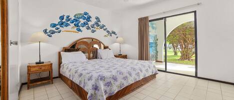 A bedroom with a bed, two bedside tables, a ceiling fan, and a view of the outdoors.