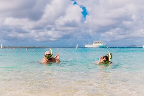 Two people snorkeling in clear turquoise water with a boat in the background. - Sand Dollar Bonaire (Kralendijk)