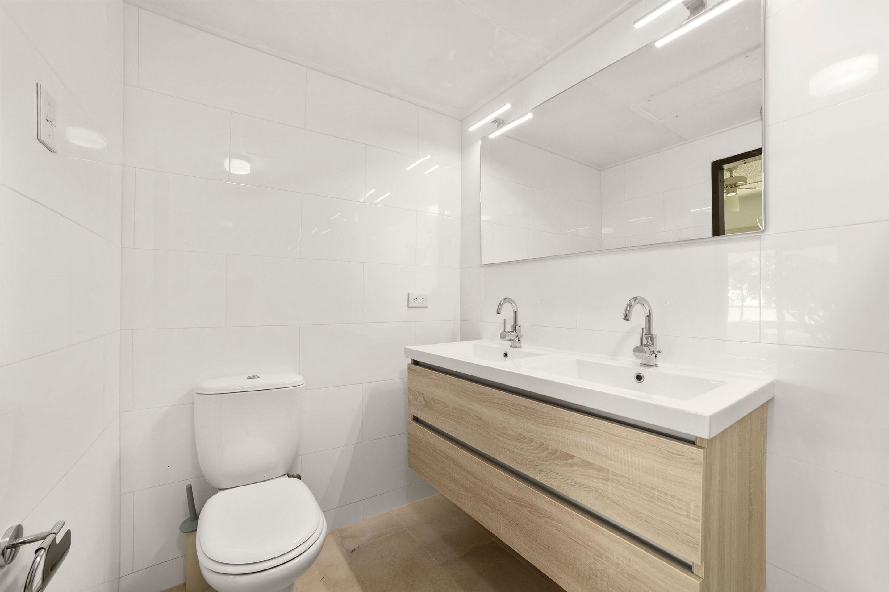 Een moderne badkamer met witte tegels, een toilet, een wastafel met spiegel en een wastafel.