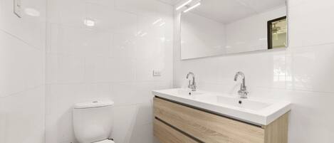 A modern bathroom with white tiles, a toilet, a vanity with a mirror, and a sink.