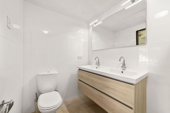 A modern bathroom with white tiles, a toilet, a vanity with a mirror, and a sink.