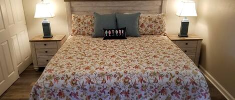 A bedroom with a floral bedspread, two nightstands with lamps, a wooden headboard, and a door.