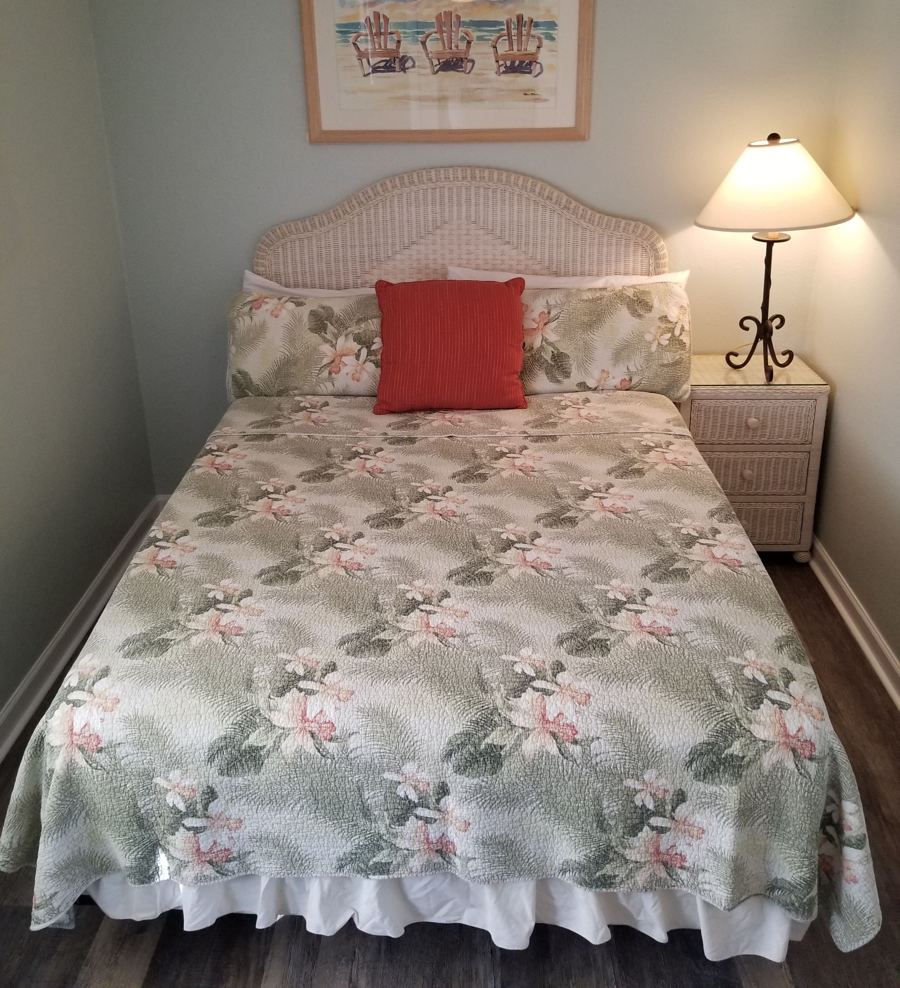 A bed with a floral-patterned bedspread, a red pillow, and a headboard with a woven design.