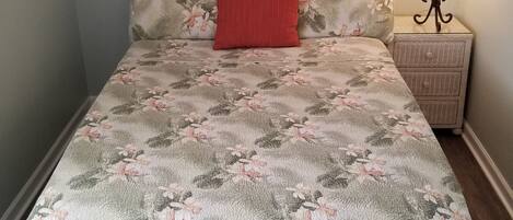 A bed with a floral-patterned bedspread, a red pillow, and a headboard with a woven design.