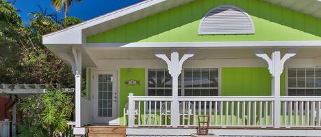 A green house with a white porch and a small garden.