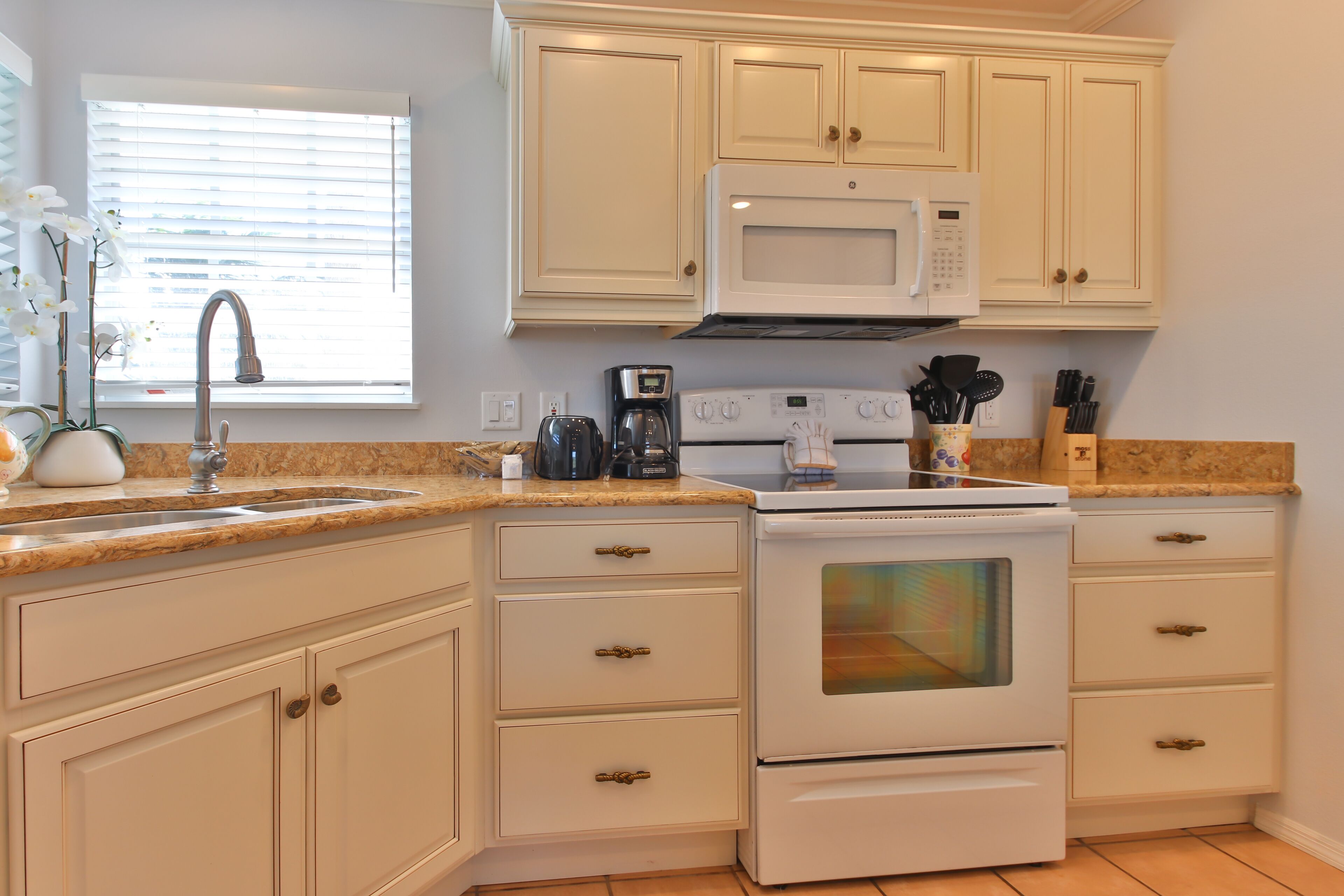 A kitchen with white cabinets, a double oven, a microwave, and a coffee maker.