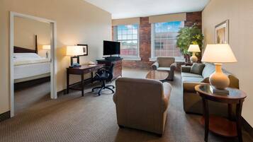 A hotel room with a bed, desk, TV, office chair, sofa, and a small table with a lamp.