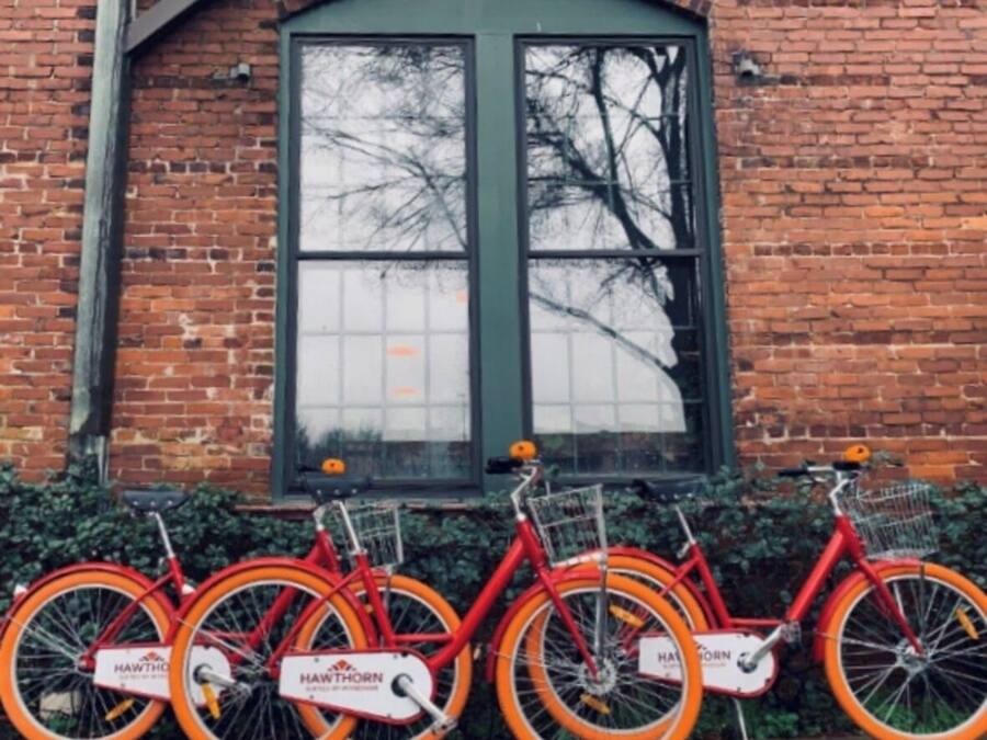 A row of red bicycles with baskets, branded "HAWTHORN," parked against a brick wall with a large window.