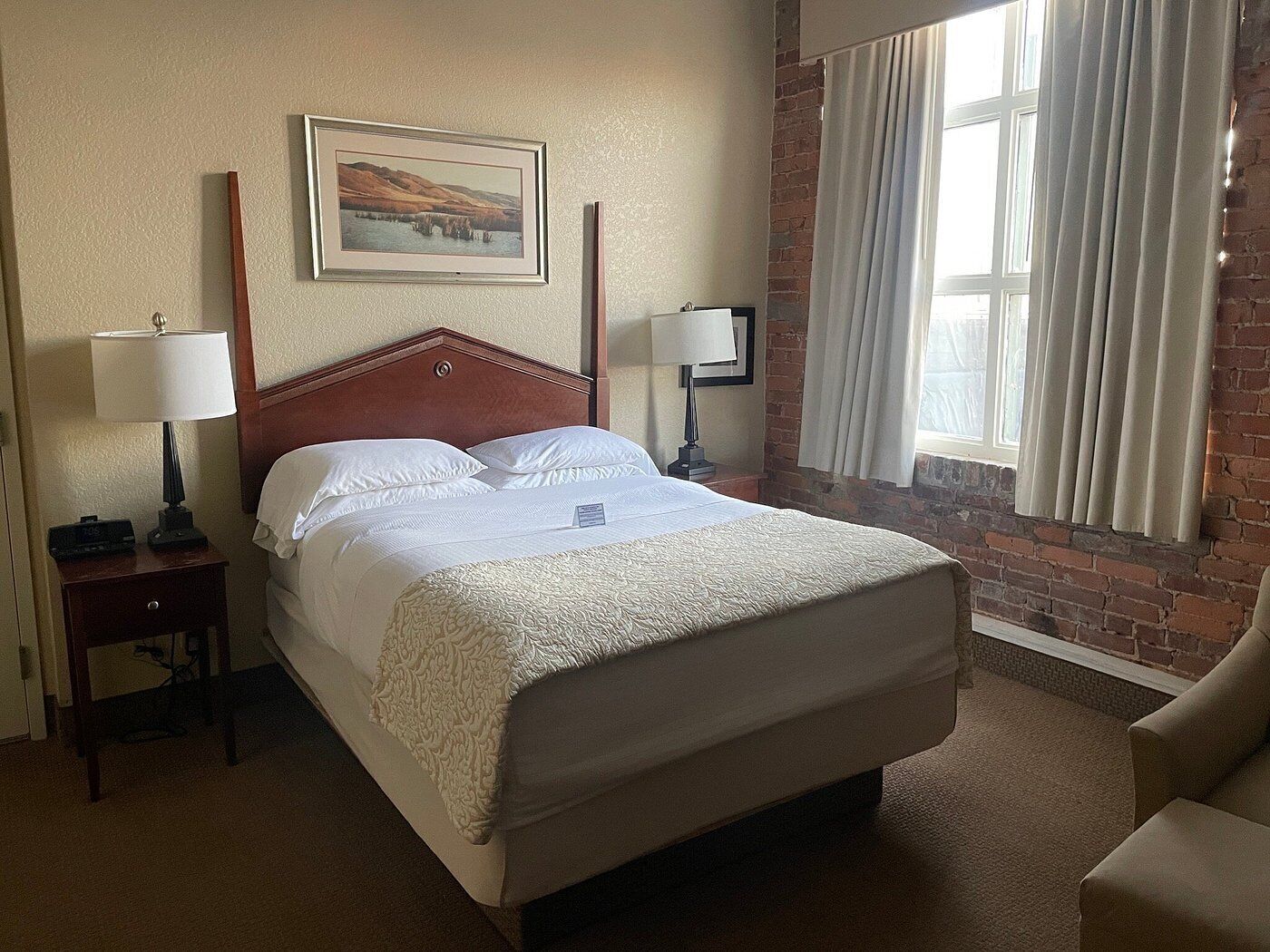 A hotel room with a large bed, two bedside tables with lamps, a framed picture on the wall, and a brick wall.