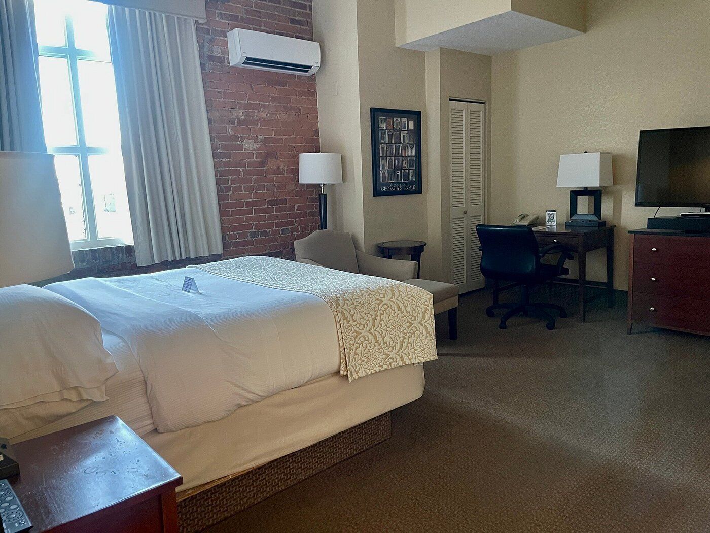 A hotel room with a large bed, a desk with a chair, a TV, and a window with curtains.