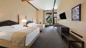 Une chambre d’hôtel avec deux lits, un bureau, une chaise, une télévision et une fenêtre donnant sur un paysage verdoyant.
