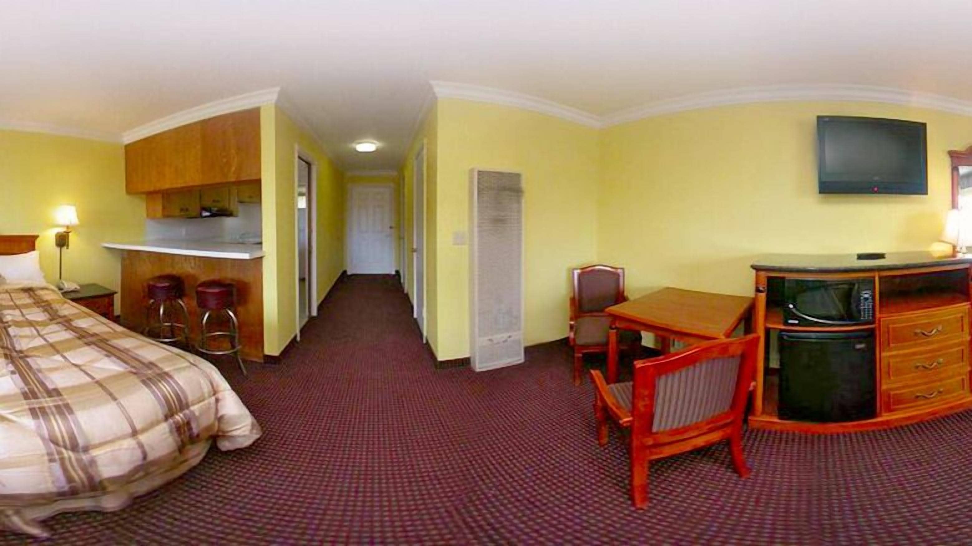 Una habitación de hotel con cama, escritorio con silla, televisión y kitchenette.
