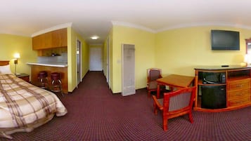 A hotel room with a bed, a desk with a chair, a television, and a kitchenette.