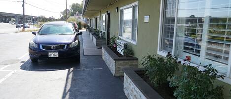 A parking lot with a car parked in front of a building with a row of windows and a planter with plants.