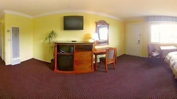 Habitación de hotel con escritorio, silla y cama. Hay un televisor montado en la pared y una ventana que proporciona luz natural.