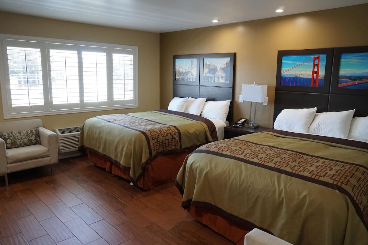 A hotel room with two beds, a sofa, and large windows.